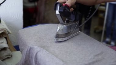 Terzi kadın eski moda ütüyle gri bir bez parçası buharlaştırıyor. Bir kadının eli demiri tutar ve kumaşı düzleştirir, ütünün buharını. Kapatın. Tanınmayan kişi