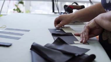 Yakın plan: Bir terzi kadın bir parça koyu renk kumaşı ütü kullanarak yapıştırıyormuş gibi buharlaştırıyor. Giysi tasarlayan bir kadın bir deseni ölçüyor ve iki parça yapıştırıyor.