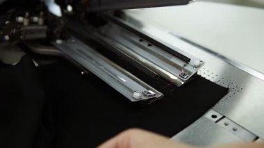 Düz dikiş dikmek için kadın elleri, siyah renkli bir tekstil makinesini otomatik dikiş makinesine koyuyor. Kadın eli, aoutomatik lazer ölçümlü dikiş makinesine dikilir. Moda, yaratım ve