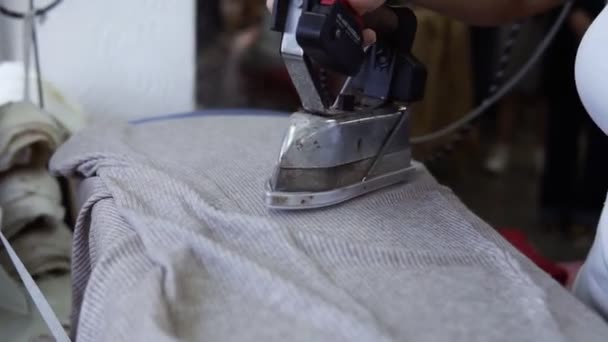 Una costurera vaporiza un trozo de tela gris usando una plancha pasada de moda. Una mano de mujer sostiene el hierro y alisa el paño, el vapor del hierro. Movimiento lento — Vídeo de stock