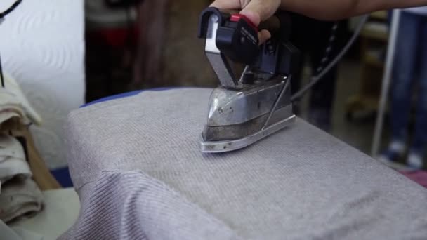 A seamstress woman steams a piece of gray cloth using an old-fashioned iron. A womans hand holds the iron and smoothes the cloth, the steam from the iron. Close up. Unrecognized person — ストック動画