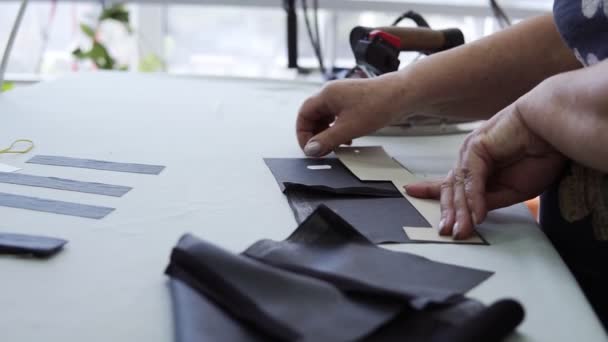 Primer plano: Una costurera vaporiza un trozo de tela oscura como pegamento, pegándolo con una plancha. Mujer dedicada al diseño de ropa que mide una pieza de patrón y se pega dos partes — Vídeo de stock