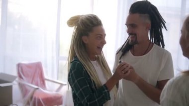 Rasta bukleli modern beyaz çift yeni evlerinin anahtarlarını emlakçıdan alıyor ve çok heyecanlanıyorlar. Yavaş çekim