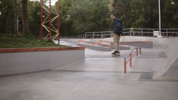 Concepto de patinadores. Joven patinador haciendo extremas patas truco mientras patina. El tipo activo disparó en el aire en un monopatín en un parque de skate, la calle de cámara lenta Kickflip. Al aire libre — Vídeo de stock