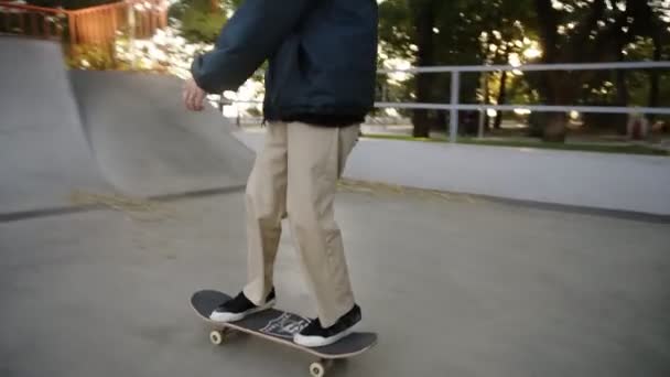Aktivní muž dělá skateboard trik na okraji skateboard rampy na skateboard kurtu, zastaví na vrcholu. Muž bruslení venku v moderním skate parku. Zelené stromy jsou na pozadí — Stock video