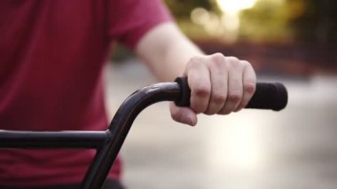 Bmx motorunun direksiyon simidi sahnesi. Kırmızı tişörtlü bir adam ellerini sürüyor. Sağlıklı, ekstrem spor yaşam tarzı. İlk insan manzarası, direksiyon, bulanık bir park manzarası. Kapat.