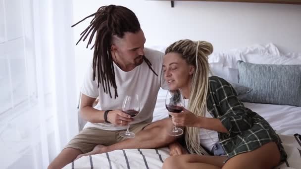 Una pareja enamorada de rastas bebiendo vino tinto de copas de vino. Clinking, disfrutando del fin de semana libre. De ocio familiar. Movimiento lento — Vídeo de stock