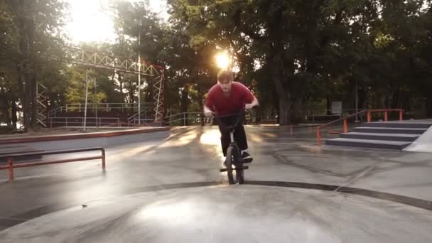 Biker Bmx exercitando com sua bicicleta ao ar livre, fazendo salto de bicicleta lado duro no parque de skate, fazendo truques no belo dia de verão. Árvores e explosões de sol no fundo — Vídeo de Stock