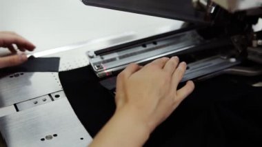 Düz dikiş dikmek için kadın elleri, siyah renkli bir tekstil makinesini otomatik dikiş makinesine koyuyor. Kadın eli dikiş makinesine dikilir. Moda, yaratım ve terzilik