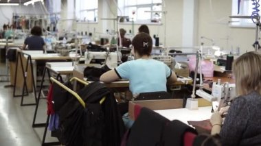 Masalardaki dikiş makinelerinde çalışan beyaz kadınlar. Endüstriyel tekstil fabrikası, üretim hattındaki işçiler, endüstriyel iç mekan, iğne dikiş makinesi. Nadir görünüm