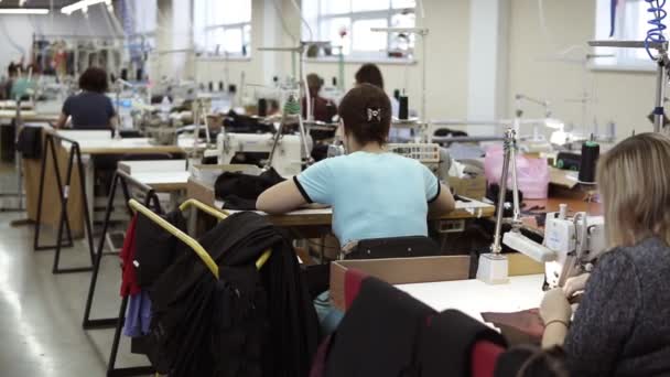 Mujeres caucásicas trabajando en una máquina de coser en las mesas. Fábrica textil de tamaño industrial, trabajadores en la línea de producción, interior industrial, máquina de coser aguja. Vista rara — Vídeo de stock