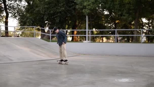 Νεαρός σκέιτερ με casual ρούχα και μαύρο καπέλο να γλιστράει από τη ράμπα και να κάνει flip trick με το board ανεπιτυχώς στο skate park. Αργή κίνηση — Αρχείο Βίντεο