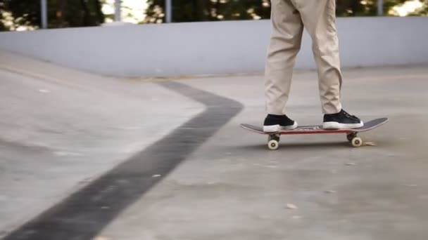 Close-up zicht op de benen van de mens in zwarte sneakers en beige broek skateboarden, inspanning in skate park. Benen op het skateboard. Langzame schot — Stockvideo