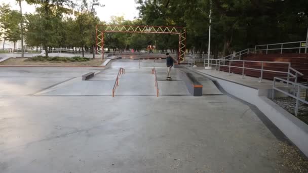 Hombre activo haciendo truco de skate en el borde de la rampa de skate en la pista de skate, se detiene en la parte superior. Hombre patinaje al aire libre en el moderno parque de skate — Vídeo de stock