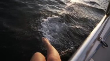 Deniz yürüyüşü sırasında yattan denize sarkan güzel kadınların bacaklarının en üst görüntüsü. Arka planda güneş ışığı ve derin mavi su var. Ağır çekimde