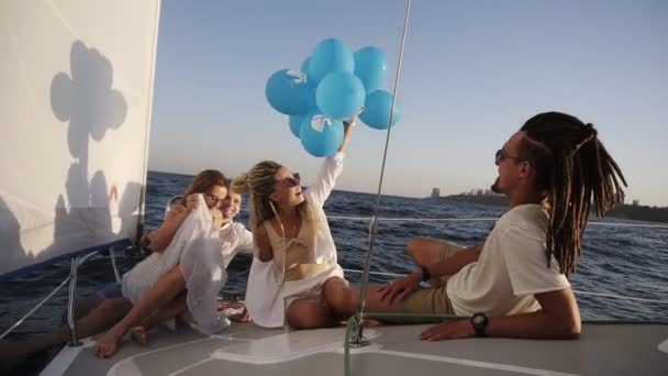 Quattro amici che fanno una crociera rilassante sullo yacht mentre sono sdraiati su un fiocco della barca. Si godono il momento - la ragazza in un bianco che agita i palloncini, festeggiando. Rallentatore — Video Stock