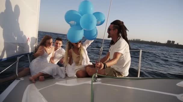 Cuatro amigos que tienen un crucero relajante en el yate mientras están acostados en una proa del barco. Ellos disfrutan del momento - chica en un blanco agitando los globos, celebrando. En cámara lenta. Día soleado pasando al aire libre — Vídeos de Stock