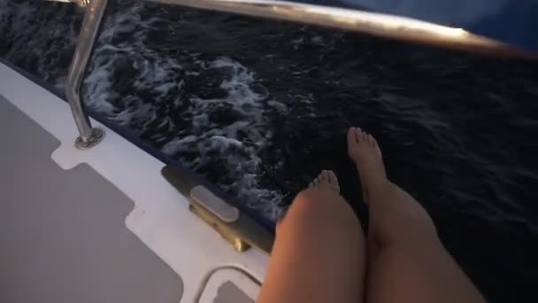 Vista superior de un agradable piernas de mujer colgando juguetonamente sobre el mar desde el yate a la luz del sol en cámara lenta — Vídeo de stock