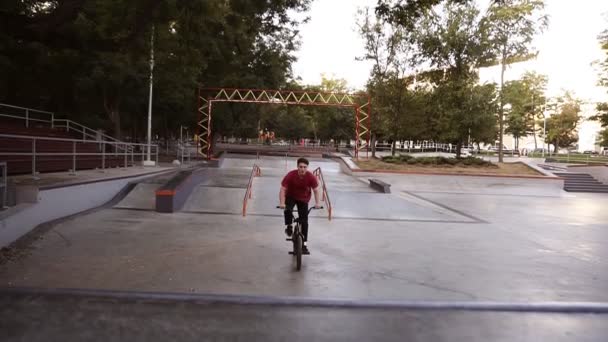 Man op Bmx fiets in openlucht skate park springen van de helling naar de lucht. Jongeman rijdt alleen in het lege sportpark. Close-up van de wielen aan de bovenkant van de oprijplaat — Stockvideo