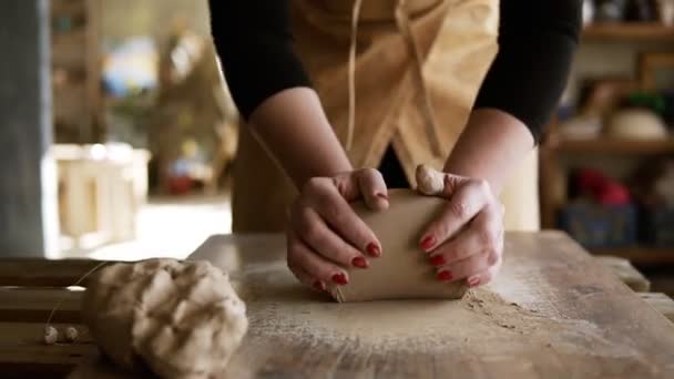 Close-up beelden van vrouwelijke handen met mooie rode manicure die klei vasthouden en kneden op een werkblad. Draagt een beige schort. Onherkenbaar persoon. Overzicht. Wazige achtergrond — Stockvideo