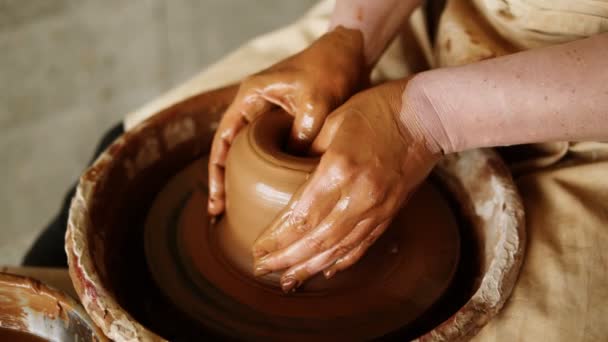 Zamknij nagranie kobiety siedzącej przy kole garncarskim w pracowni ceramicznej kształtującej gliniany wazon - zanurzającej palce w środku. Osoba nierozpoznawalna — Wideo stockowe