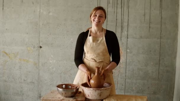 Glada kvinna håller färdig, rå vas av lera. Porträtt av kvinnlig krukmakare, hon arbetar i en keramikverkstad med lera. Begreppet keramik mästerskap och kreativitet — Stockvideo