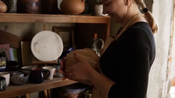 Радостная, современная женщина-гончар берет вазу ручной работы с полки в студии, довольна своей работой, улыбается и довольна идеальной формой — стоковое видео