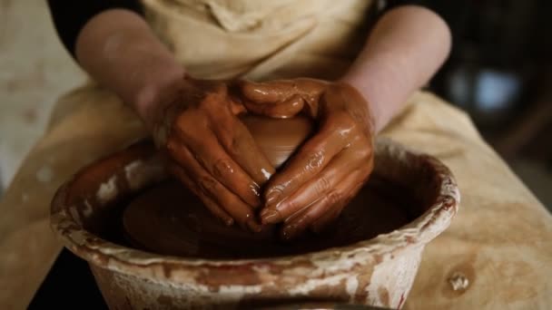 Retrato de jovem mulher bonita vestindo avental sentado em cerâmica e fazendo vaso de barro na roda de oleiro usando as mãos. Mulher sorrindo para uma câmera — Vídeo de Stock