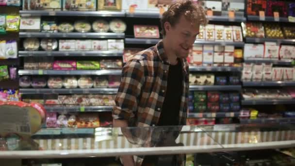 Portret van een knappe man in een geruit hemd die rondloopt en rondkijkt in de supermarkt. Rijpere man in de 30 op zoek naar producten tijdens het winkelen in de supermarkt. Staren naar showcase — Stockvideo