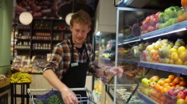Süpermarkette siyah önlük giyen yakışıklı bir borsacı organik meyve ve sebze düzenliyor. Rafa taze kırmızı elmalar ekliyorum. Yavaş çekim