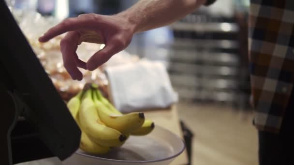 Tema kesehatan dan makanan alami. Close-up dari tangan seorang pria mengenakan pisang pada skala. Pria kulit putih yang menimbang setumpuk pisang. Seorang pria vegetarian membeli buah kuning — Stok Video