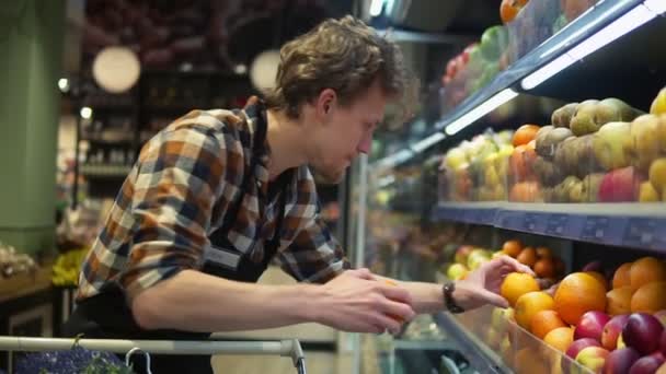 Im Supermarkt: Eine hübsche Verkäuferin mit schwarzer Schürze sortiert Bio-Obst und -Gemüse. Frische Orangen ins Regal. Zeitlupe — Stockvideo