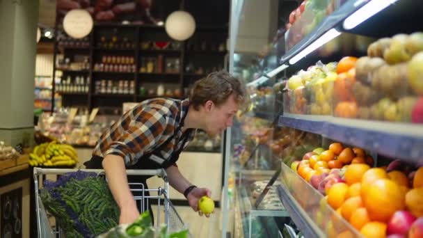 En el supermercado: Guapo empleado de bolsa con delantal negro, organizando frutas y verduras orgánicas. Añadir manzanas frescas en el estante de la tienda. Movimiento lento — Vídeos de Stock