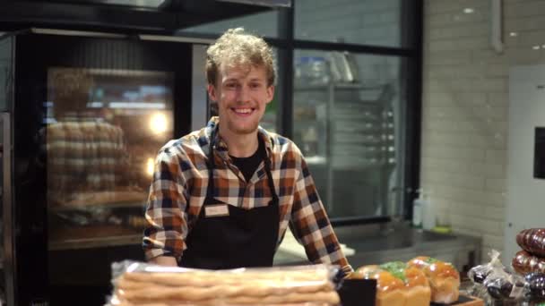 Portrait du bel homme boulanger en chemise à carreaux et tablier souriant à la caméra et posant dans la boulangerie. Ferme là. Intérieur — Video