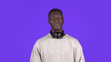 Beyaz gömlekli, kulaklıklı çekici genç bir adam mavi arka plan üzerinde başını sallıyor.
