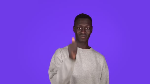 Usmívající se pozitivní mladý africký Američan muž v bílém svetru dělá palec-up gesto izolované přes modrou zeď pozadí ve studiu — Stock video