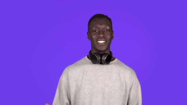 Attractive joyful young african man looking to the camera in headphones on neck smile happy talks at camera. Positive emotions. Male portrait. Contemporary human — Stock Video