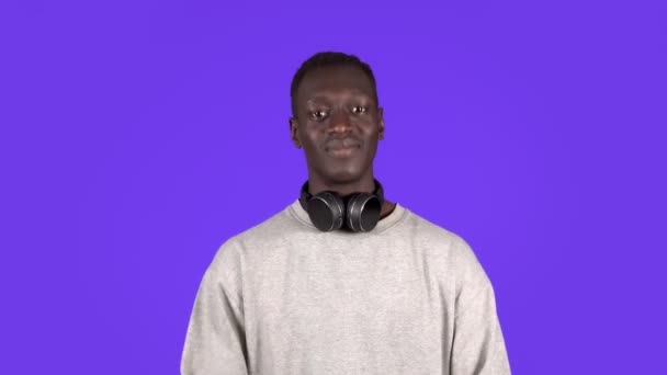 Un giovane uomo attraente con le cuffie sul collo in camicia bianca annuisce la testa positivamente isolato su sfondo blu — Video Stock