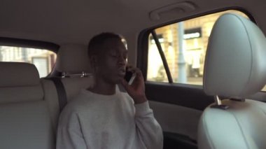 Taksinin arka koltuğunda otururken cep telefonuyla konuşan rahat ve yakışıklı Afrikalı bir adam. Neşeli siyahi yolcu şehir gezisi sırasında telefonlara cevap veriyor.