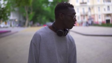 Gözlüklü, kameraya bakıp gülümseyen Afrikalı Amerikalı genç bir adamın portresi mutlu ol. Sırt çantasını tak, mutluluk modası insanları yakışıklı, çekici, yavaş çekimli, şehir dışı şehirli insanlarla yüzleştir.