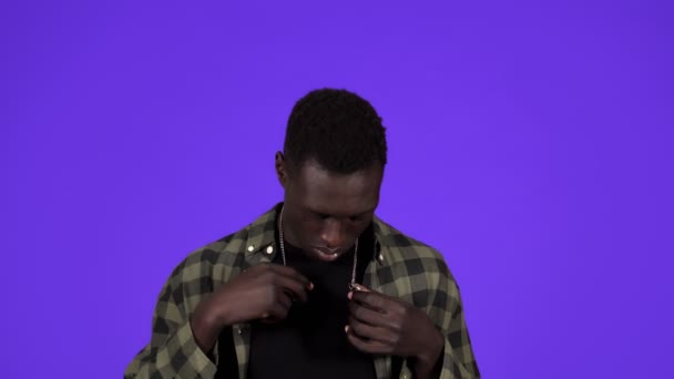 Afrikai férfi portré kék háttérrel. Gazdagság, hiúság, büszkeség, arrogancia. Egy alkalmi fickó próbálja lezárni az arany láncot a nyakán. — Stock videók