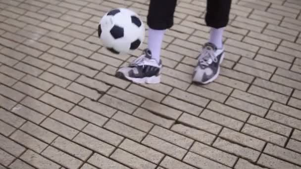 Un joven afroamericano lanza una pelota de fútbol con los pies. Un tipo con auriculares calentándose al aire libre, jugando al fútbol. Hombre despreocupado divertirse al aire libre — Vídeos de Stock