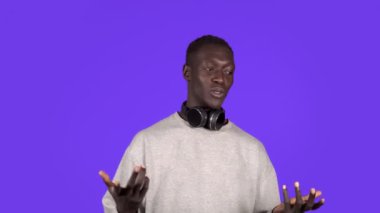 Çekici, neşeli, Afrikalı bir adam kameraya boynunda kulaklıkla bakıyor. Gülümsüyor, kameraya konuşuyor, bir şeyler anlatıyor. Olumlu duygular. Erkek portresi. Çağdaş insan