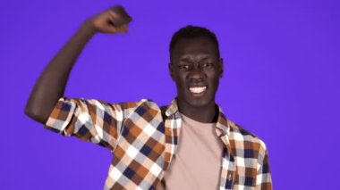 Sade tişört giyen güçlü Afro-Amerikan genç adam stüdyoda mavi arka planda kameraya kaslarını gösteriyor, sporcu. İnsanlar samimi duygular, yaşam tarzı konsepti