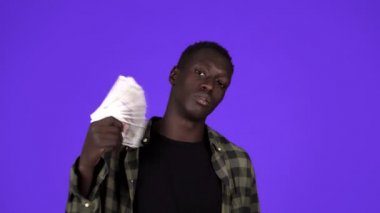 Mutlu Afrikalı Amerikalı adam elinde 100 dolarlık banknotlar tutuyordu. Stüdyoda mavi arka planda poz verirken başını sallayıp kameraya bakıyordu.