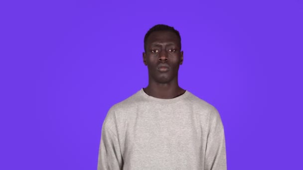 Retrato de um jovem homem sério a olhar para a câmara com braços cruzados a protestar. Belo homem negro africano em camisola branca no fundo azul — Vídeo de Stock
