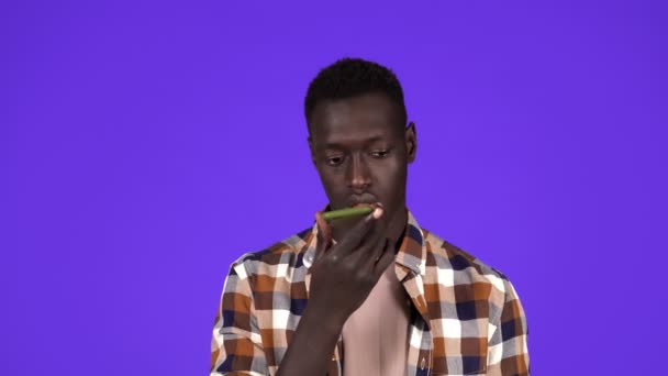 Een intelligente technologie. Jonge man in geruite shirt praten met smartphone met behulp van digitale voice app om gegevens te zoeken, online bestellen, luisteren antwoord. Studio shot geïsoleerd op blauwe achtergrond — Stockvideo