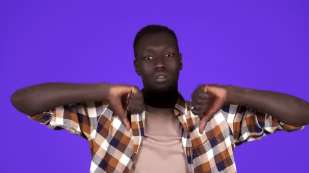 Pria muda berkulit hitam serius menunjukkan sikap menolak dengan jempol ke bawah tidak setuju berdiri negatif di latar belakang biru. Ekspresi manusia — Stok Video