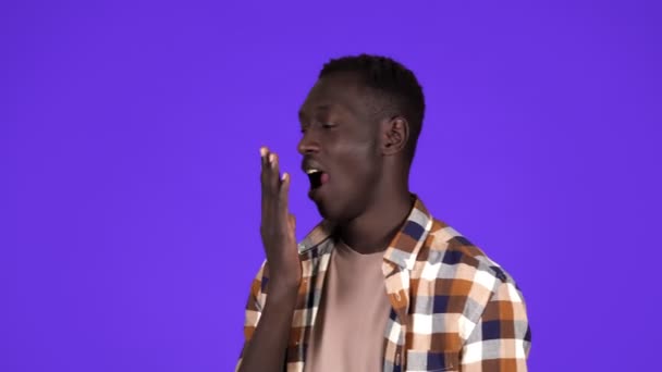 Un joven afroamericano de pelo corto está bostezando, tocando su cara, cansado y soñoliento de pie aislado sobre el fondo de la pared azul en el estudio. Vista lateral — Vídeos de Stock