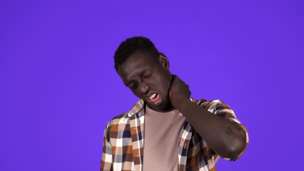 Giovane uomo afroamericano in camicia scozzese con dolore al collo o super stanco, faccia smorfia. isolato su sfondo blu — Video Stock